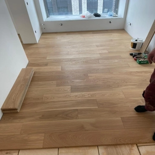 Light wood-look PVC floorings being installed in a room, with stacked planks ready for fitting.