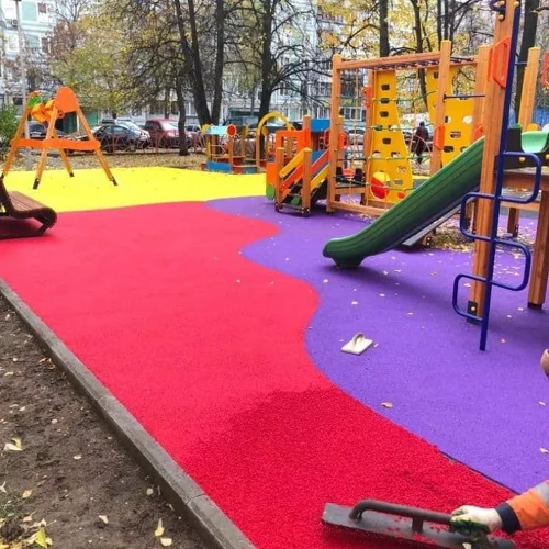 Vibrant playground with red, purple, and yellow rubber flooring being installed, featuring slides, climbing frames, and swings—ideal for safe and colorful outdoor play.