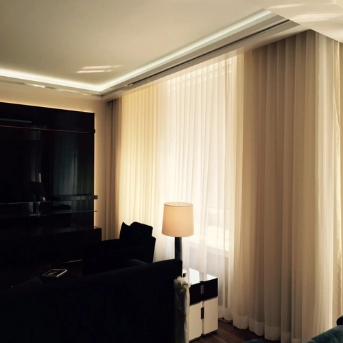 Warmly lit room with full-length cream curtains and a floor lamp.