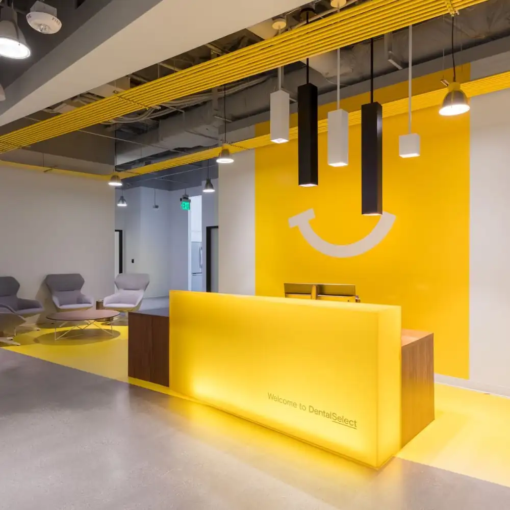 A bright dental clinic reception with a yellow backlit desk and wall.