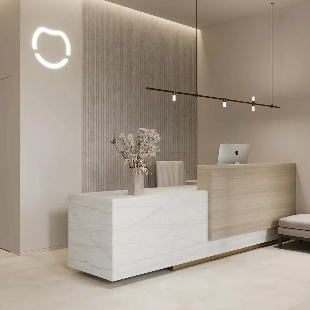 A minimalist and elegant reception area featuring a two-tone desk. The front of the desk is a white marble block, while the side is light wood with a gold metal base.