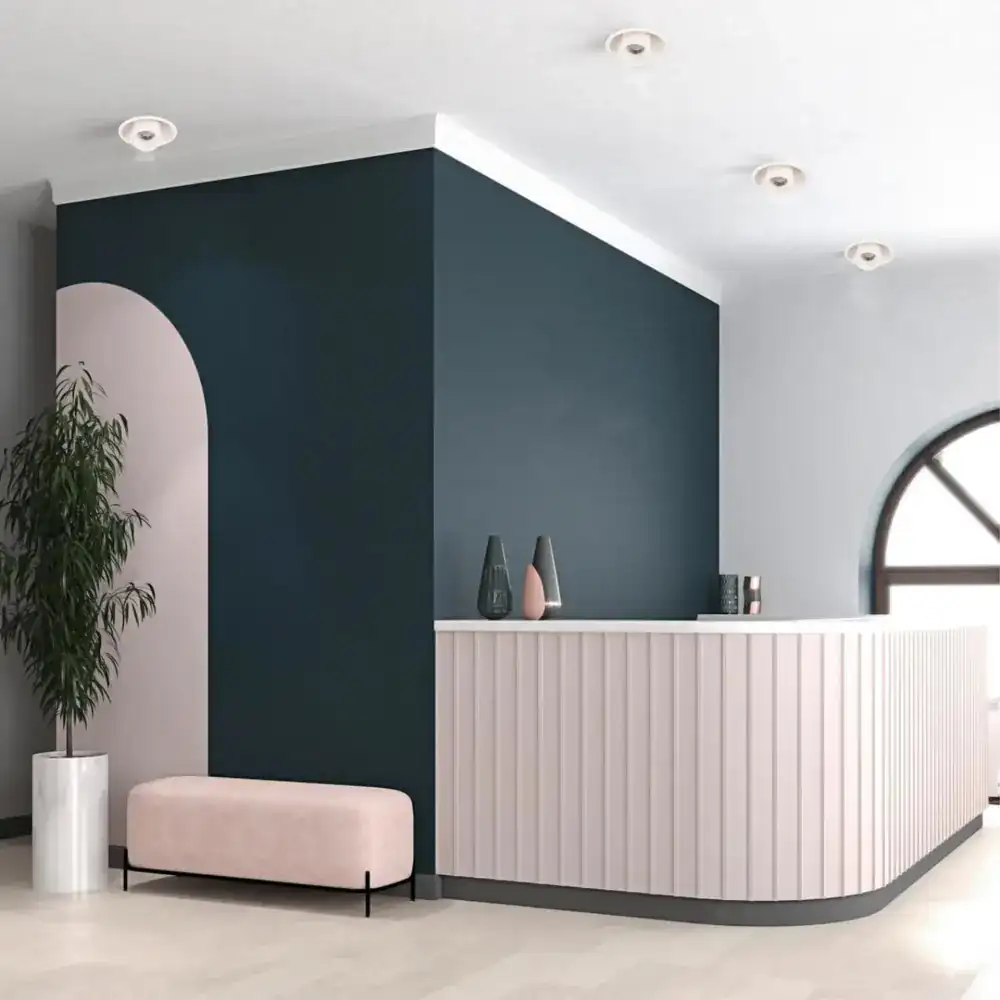 A stylish reception with a curved, light pink desk and dark blue wall.